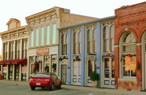 Historic storefronts adorned with holiday decorations, featuring a red car parked in front.
