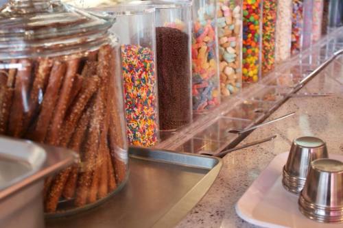 A variety of colorful candies and sprinkles in jars, with pretzels in a glass container on a countertop.