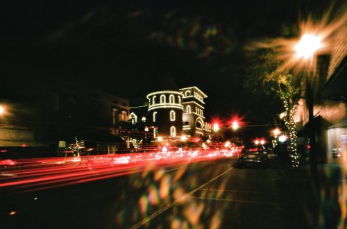 A nighttime street scene with a beautifully lit building and streaks of car lights creating a festive atmosphere.