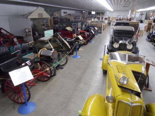 A vintage car museum featuring various classic cars and carriages displayed in a spacious indoor setting.
