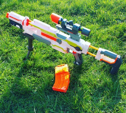 A colorful toy rifle with a scope and detachable magazine, resting on green grass.