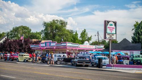 A vibrant diner with classic cars parked outside, surrounded by people enjoying a sunny day.