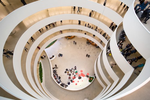 Aerial view of a spiral staircase in a modern building, with people gathered on the lower level.