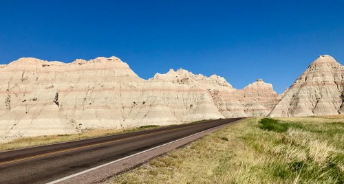 A scenic view of a winding road alongside colorful, layered rock formations under a clear blue sky.