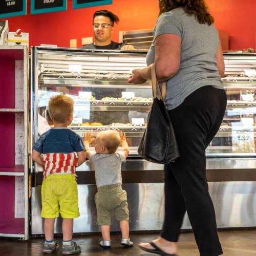 A woman and two young children look at a display case filled with pastries in a colorful bakery.