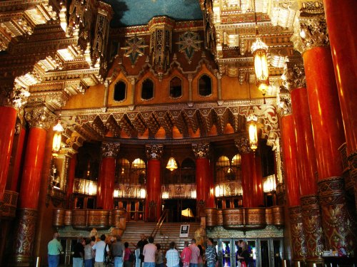 Interior of a grand theater with ornate architecture, featuring tall columns, intricate designs, and a staircase.