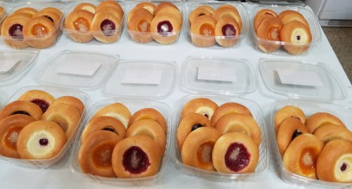 A display of assorted donuts in clear plastic containers, featuring various fruit fillings and glazes.