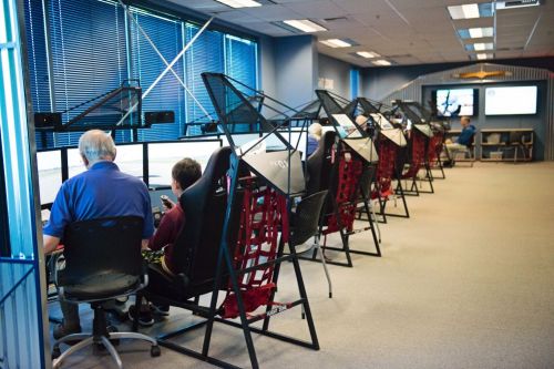 A room with several flight simulators, where individuals are seated and engaged in simulation activities.