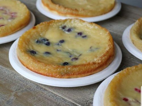 Several round, golden-brown baked desserts with a creamy filling and scattered blueberries on white plates.