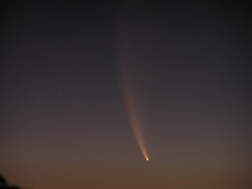 A comet streaks across a twilight sky, leaving a glowing tail against a gradient of dark blue and purple hues.