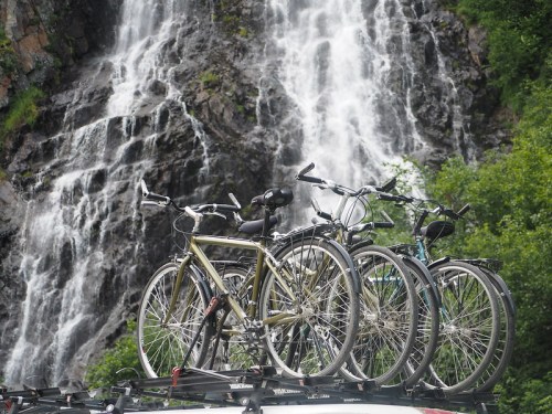 Bicycles on a car roof rack with a waterfall and lush greenery in the background.
