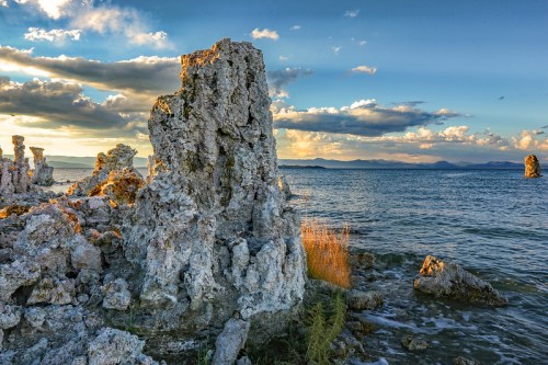Rocky formations rise from the water under a colorful sky, with clouds reflecting the sunset over the lake.