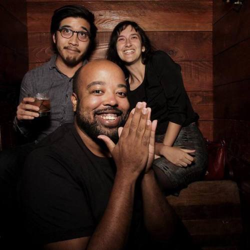 Three friends pose together in a cozy setting, smiling and enjoying each other's company. One holds a drink.