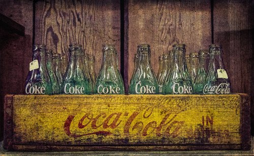 Vintage Coca-Cola bottles arranged on a wooden crate with faded branding, set against a rustic wooden background.