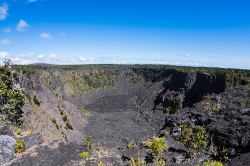 A panoramic view of a volcanic crater surrounded by lush greenery and a clear blue sky.