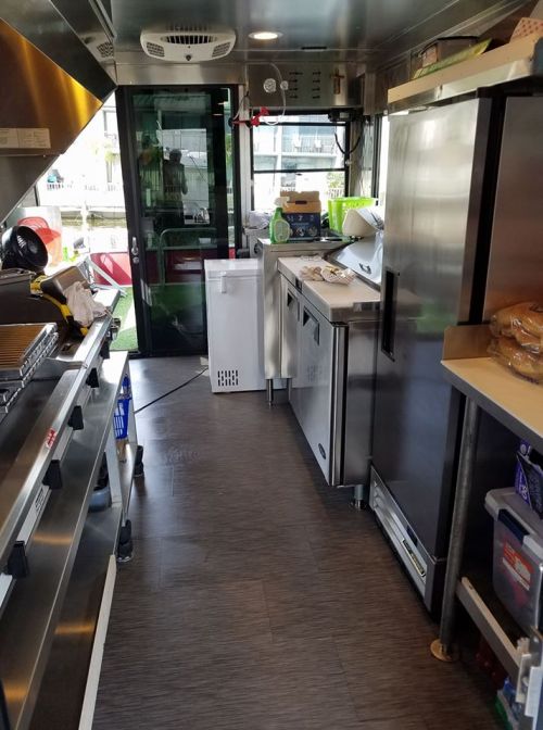 Interior of a food truck featuring stainless steel appliances, a grill, and organized workspace.