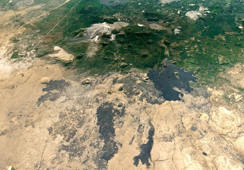 Aerial view of diverse terrain featuring green forests, rocky areas, and volcanic craters in a landscape.