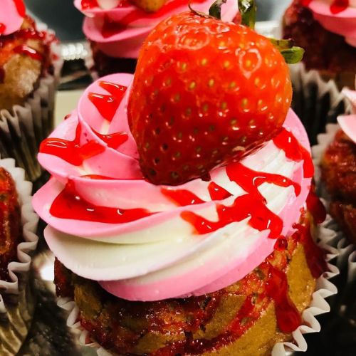 Close-up of a cupcake topped with pink frosting, a fresh strawberry, and a drizzle of red syrup.