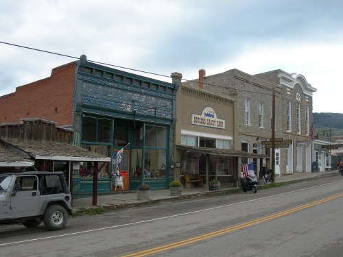 Historic buildings line a small town street, featuring shops and a vintage jeep parked nearby.