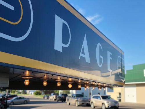 Signage for "PAGE" with decorative lights, set against a clear blue sky and buildings in the background.