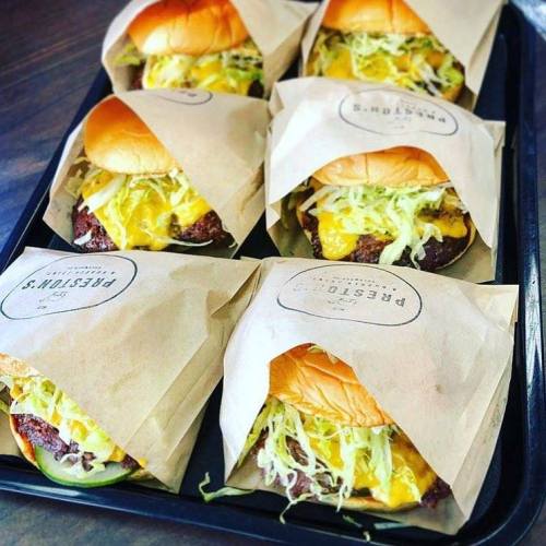 A tray of six wrapped burgers with cheese, lettuce, and pickles, presented in brown paper packaging.