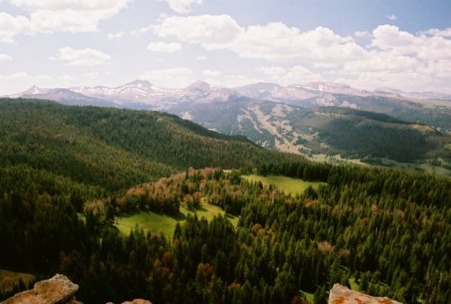 A panoramic view of lush green forests and distant mountains under a partly cloudy sky.