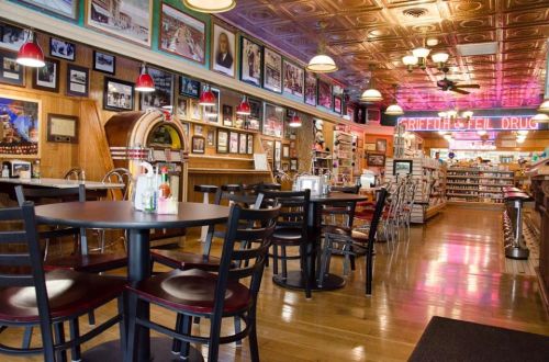 A vintage diner interior with wooden tables, a jukebox, and walls adorned with framed photos and memorabilia.