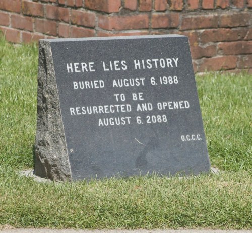 A dark stone grave marker reads: "Here lies history, buried August 6, 1988, to be resurrected August 6, 2088."
