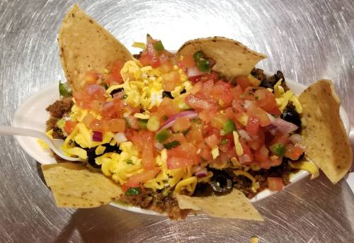 A bowl of nachos topped with ground beef, cheese, diced tomatoes, olives, and tortilla chips.