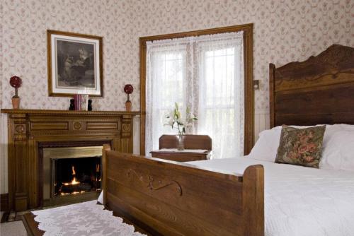 Cozy bedroom with a wooden bed, floral wallpaper, a fireplace, and a vase of flowers on a bedside table.