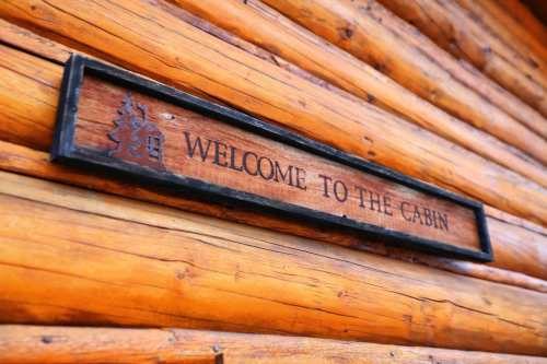 Wooden sign reading "Welcome to the Cabin" mounted on a rustic log wall.