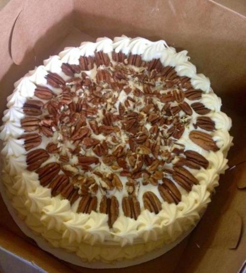 A round cake topped with cream frosting and decorated with pecans, placed in a cardboard box.