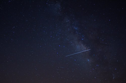 A starry night sky featuring the Milky Way and a bright meteor streaking across the scene.