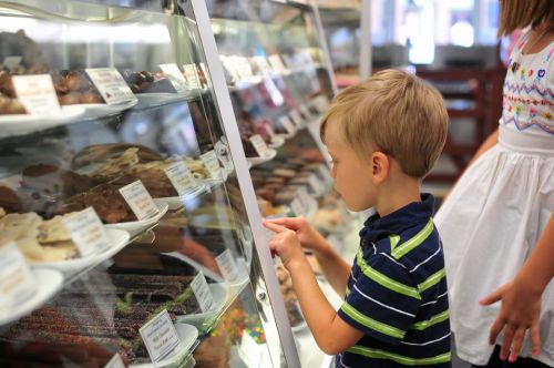 A young boy points at a display case filled with various sweets and treats, while a girl stands nearby.
