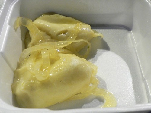 Two dumplings topped with translucent onion slices in a white takeout container.