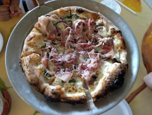 A freshly baked pizza topped with prosciutto, cheese, and vegetables, served on a metal tray.
