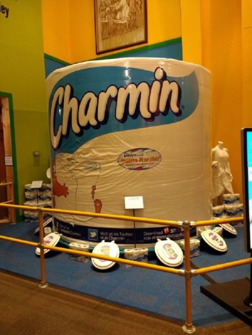 Giant Charmin toilet paper roll display in a colorful exhibit, surrounded by smaller toilet paper products.