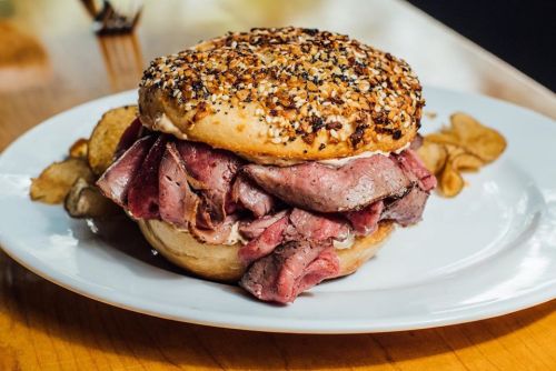 A hearty sandwich piled high with roast beef on a sesame seed bun, served with crispy potato chips on the side.