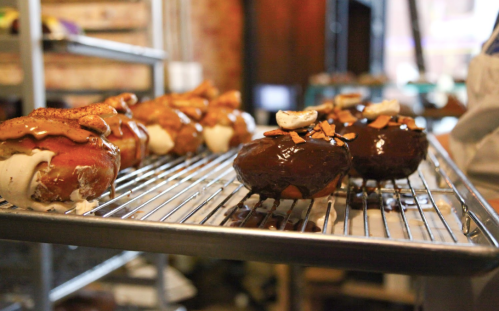 A tray of gourmet donuts, some topped with chocolate glaze and others with caramel and nuts, on a cooling rack.