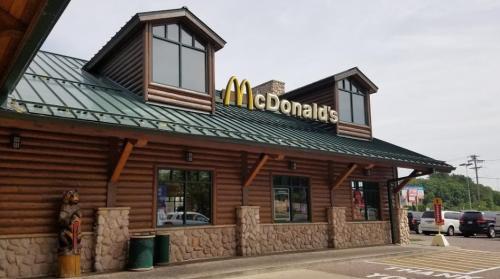 A McDonald's restaurant with a log cabin design, featuring a green roof and large windows.