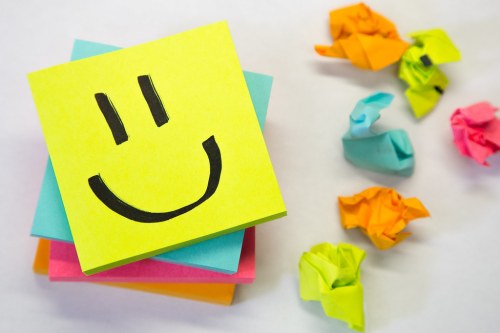 A stack of colorful sticky notes with a smiley face, surrounded by crumpled paper in various colors.
