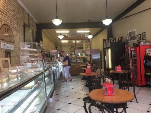 A cozy bakery interior with display cases, tables, and customers browsing desserts. Warm lighting and vintage decor.