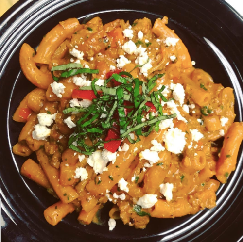 A plate of pasta with a creamy tomato sauce, topped with fresh basil, red peppers, and crumbled cheese.