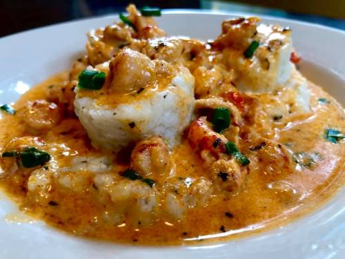A plate of creamy shrimp and rice, garnished with green onions in a rich sauce.