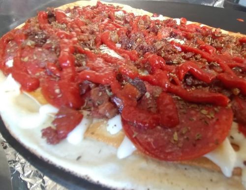 A close-up of a loaded pizza with pepperoni, bacon, herbs, and drizzled with ketchup on a flatbread base.