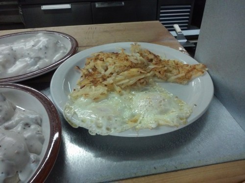A plate with two fried eggs and crispy hash browns, served in a casual dining setting.