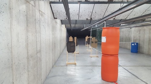 Indoor shooting range with targets on stands, orange barrels, and concrete walls.