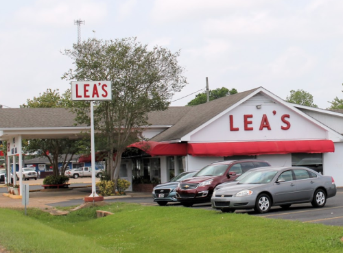 A restaurant named "Lea's" with a red awning and sign, surrounded by parked cars and greenery.