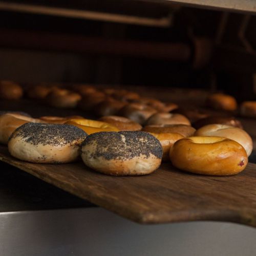Freshly baked bagels on a wooden board, featuring poppy seed and plain varieties, in a warm, inviting bakery setting.