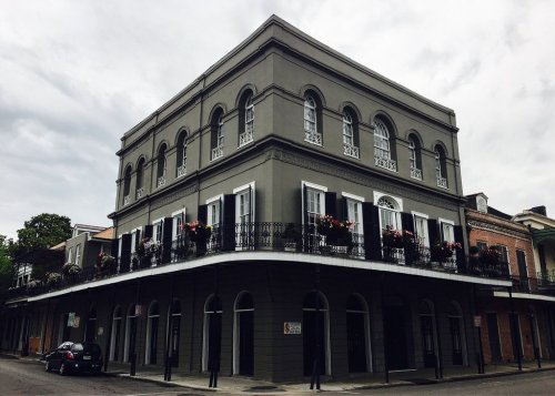 Historic gray building with arched windows and balconies adorned with flowers, set against a cloudy sky.